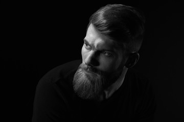 Dramatic concept Black and white close-up portrait of young handsome bearded man looking forward. Studio shot on black background