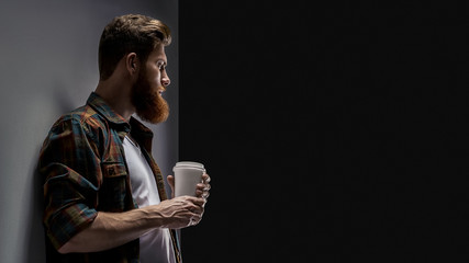 Close up shot of side view of young bearded man drinking cappuccino coffee Coffee on the go studio shot on black background Free space for brand corporate, mockup template