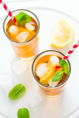 Glasses of iced tea with lemon slices and mint on white wooden background