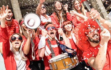 Young football supporter fans cheering with flag and confetti watching soccer match at stadium - Friends people group with red t-shirts having excited fun on sport world championship concept