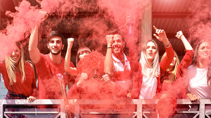Young football supporter fans cheering with colored smoke watching soccer match together at stadium...