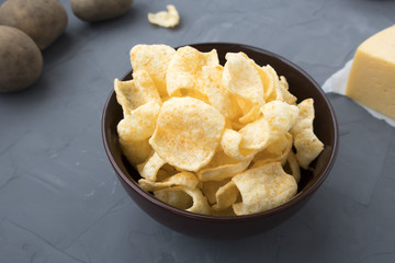 Potato chips with cheese in a plate that is located on a gray background.