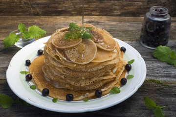 Pancakes are located in a plate on an old wooden table decorated with berries and mint leaves. Pancakes water honey.