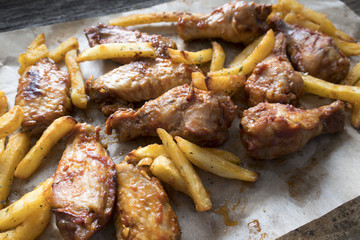 Appetizing fried pieces of chicken, pieces of chicken wings and fried potatoes located on paper and close-up