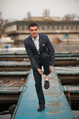 Young man walks along pier and rolls up his trousers on his leg.