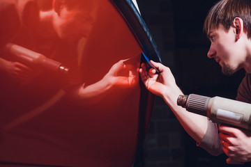 Car wrapping specialist putting vinyl foil or film on car. cutting protective film with torch. wrapping yacht, boat, ship, car, mobile home. orange film