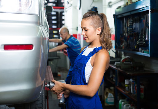 woman technician fitting new tires to car at workshop