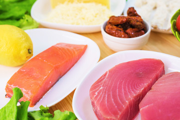 Raw appetizing fillet of tuna on a table with a yard of Greek salad with salmon and lemon cucumbers and tomatoes as well as cheese. The concept of a delicious and healthy home-made meal