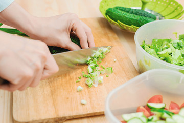 Close-up of gentle female hands slice on the wooden board the stalks of green onions making salad. The concept of a vegetarian healthy food and lifestyle. Making healthy food at home