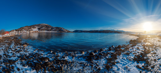 Panoramic view of beautiful winter lake with snowy mountains and sun shining at Lofoten Islands in Northern Norway