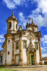Fototapeta premium Facade of the church of São Francisco de Paula in Ouro Preto, Minas Gerais with its windows, large wooden door, stone arch, towers, and baroque sculptures