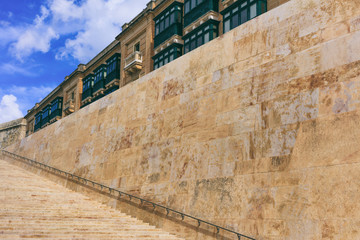 Stone stairs and wall with metal rail in the historic center of Valletta, Malta. Blue sky and traditional Maltese buildings background