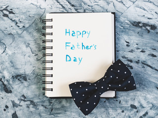 Silk bow tie and sketchbook with handwritten greeting on Father's day on a beautiful, grey table. View from the top. Concept of a happy family, fashion and elegance