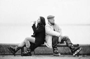Roller skating. Black and white photo. A girl on rollers drinks water from a bottle. Sport and water. Father and daughter on a bench. Active old people. © shchus
