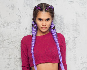 The beautiful girl looks thoughtfully and seriously into the camera. Purple braids and a red outfit. Close-up.