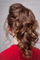 Hairstyle East tail on the head brown-haired side view against a white brick wall close-up.Professional women's hairstyle.