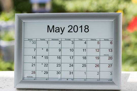 Close-up: calendar of the month of May 2018 with holidays and lunar days on a blurred background of green nature in a garden on a sunny day.
