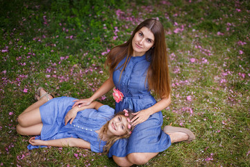 Fototapeta premium Portrait of beautiful mother and her little pretty daughter on meadow with sakura petals