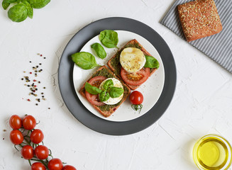 Sandwich with mozzarella cheese and red tomatoes, basil leaves, pepper, olive oil, gray plate, healthy breakfast, food concept, white background
