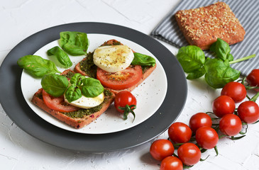 Sandwich with mozzarella cheese and red tomatoes, basil leaves, pepper, olive oil, gray plate, healthy breakfast, food concept, white background