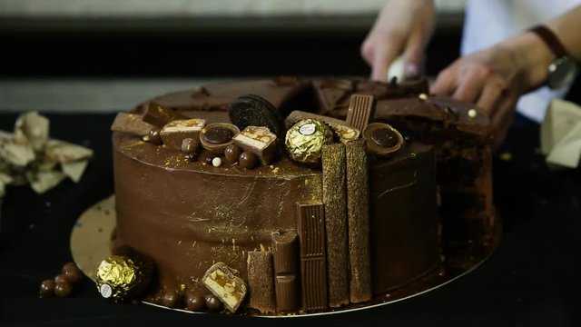 confectioner hands cut by knife big fabulous chocolate cake decorated with candies and sprinkled with food gold
