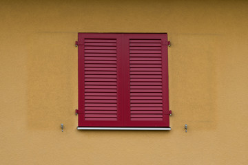 Red wooden shutters on a building with yellow painted walls.