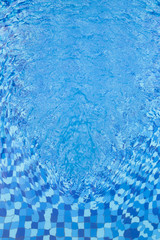 Abstract full frame background of rippled water and blue swimming pool mosaic tiles, viewed from above.