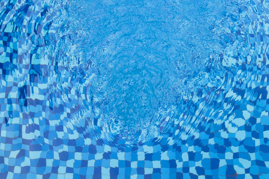Abstract full frame background of rippled water and blue swimming pool mosaic tiles, viewed from above.