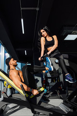 Obraz na płótnie Canvas Personal trainer helping a men working out on leg press machine in gym