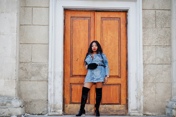 Fototapeta na wymiar African american girl in jeans dress posed on streets of city. Black stylish model shoot.