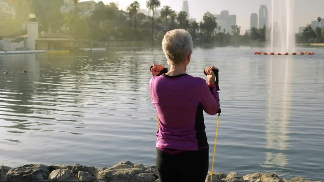 71 year old woman working out in the park with resistance bands.