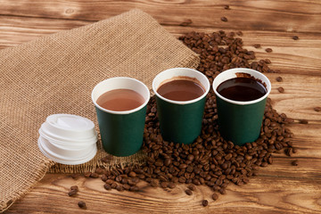 Obraz na płótnie Canvas Three take away green paper cups with coffee beans and hot chocolate drink on wooden background, top view, close-up