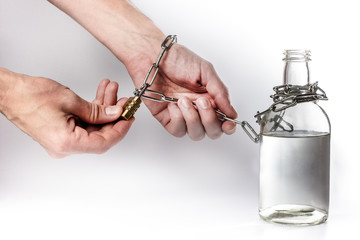 the man's hands are tied to the bottle with a metal chain with a lock. the concept of getting rid of alcohol dependence