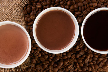Three take away green paper cups with coffee beans and hot chocolate drink on wooden background, top view, close-up