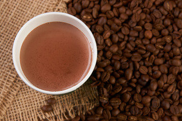 Take away coffee paper cup with hot chocolate drink and roasted coffee beans on wooden table background with copy space, top view, close-up