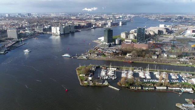 Aerial footage of Amsterdam moving left over IJ the ferries moving over water and looking towards the west side showing Central Station to the left and former Shell headquarters to the right side 4k