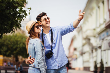 Happy young couple of tourists on vacations searching a street in a map and pointing away