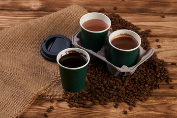 Three cardboard coffee cups. Take away green paper cups with coffee beans and hot chocolate drink on wooden background