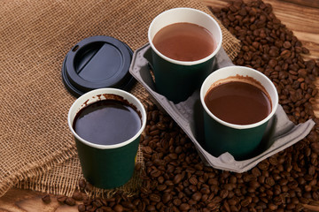 Three cardboard coffee cups. Take away green paper cups with coffee beans and hot chocolate drink on wooden background
