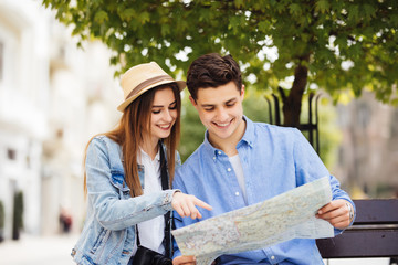 Checking some information in the guidebook. Couple sitting on bench and looking in map in new city