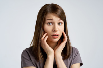 alarmed and worried young woman, the brunette looks scared in the camera and brings her palms to the cheeks. 