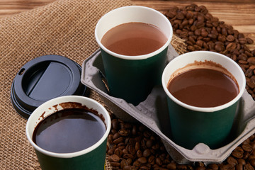 Three cardboard coffee cups. Take away green paper cups with coffee beans and hot chocolate drink on wooden background