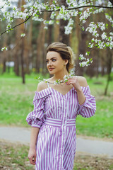 Beautiful blonde girl with blond hair in a dress on a background of spring blooming trees