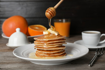 Pouring honey onto delicious pancakes with butter on table
