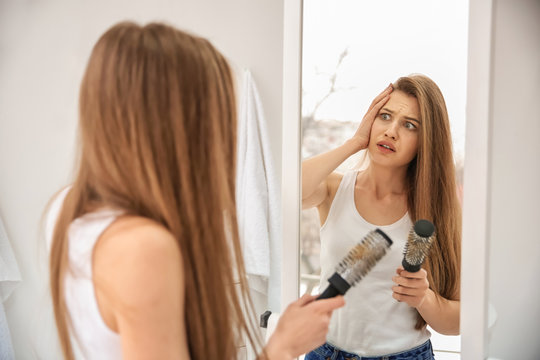 Young woman with hair loss problem looking in mirror indoors