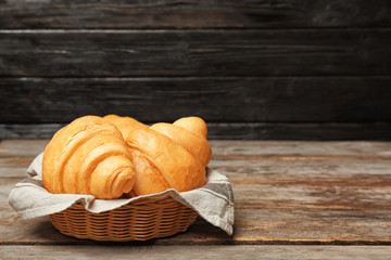 Basket with tasty croissants on wooden table