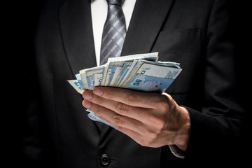 Close up of man in black suit holding a lot of cash on black background