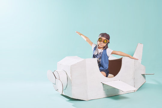 Little cute girl playing with a cardboard airplane. White retro style cardboard airplane on mint green background . Childhood dream imagination concept .