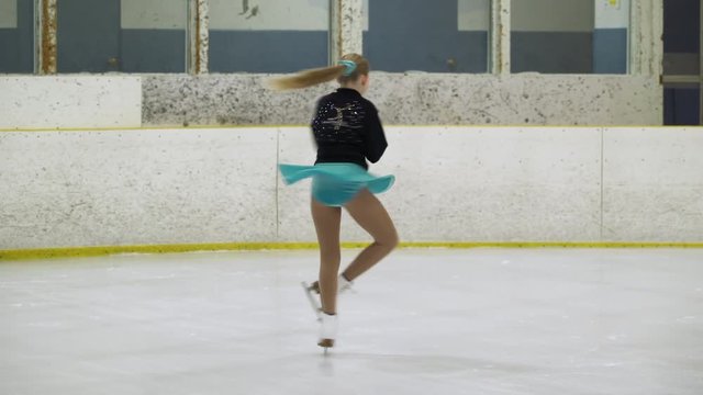 Young girl spinning round on ice skates on one leg on ice rink.