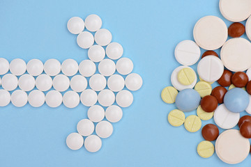 arrow of white pills and stack of tablets  on a blue background